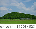A Series H100 train runs against the backdrop of a hill covered in fresh greenery. 142034623