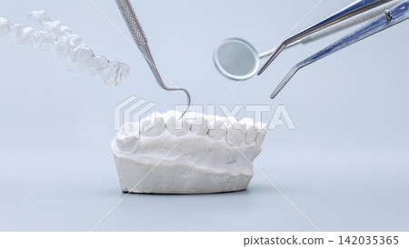 Levitating dental instruments, clear aligner, and white plaster jaw model on a light blue background. Levitating dental instruments, clear aligner, and white plaster jaw model on a light blue background. 142035365