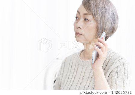 Senior woman talking on her smartphone in the living room Senior woman talking on her smartphone in the living room 142035781