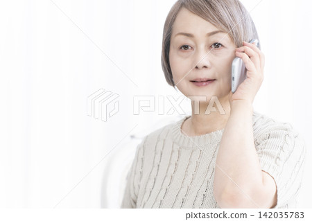 一位老婦人在客廳用智慧型手機通話 一位老婦人在客廳用智慧型手機通話 142035783