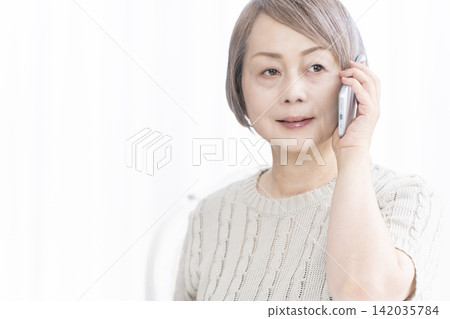 一位老婦人在客廳用智慧型手機通話 一位老婦人在客廳用智慧型手機通話 142035784