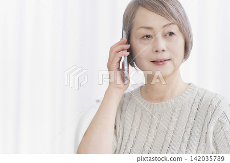 一位老婦人在客廳用智慧型手機通話 一位老婦人在客廳用智慧型手機通話 142035789