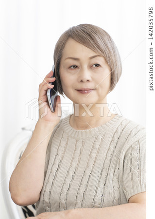 Senior woman talking on her smartphone in the living room Senior woman talking on her smartphone in the living room 142035798