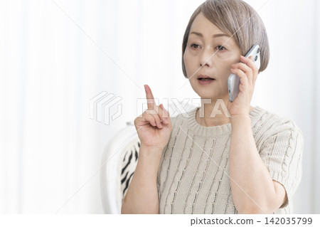 Senior woman talking on her smartphone in the living room Senior woman talking on her smartphone in the living room 142035799
