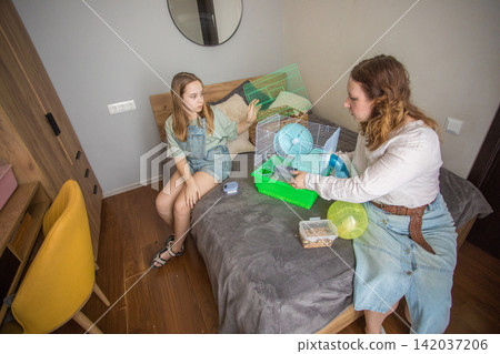 Mom and girl sit on a bed in a small room with pet. Mom and girl sit on a bed in a small room with pet. 142037206