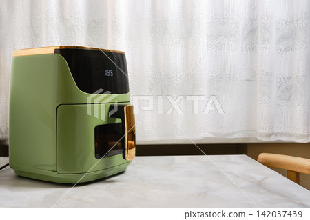 Air fryer on kitchen table near window with sheer curtains in daytime Air fryer on kitchen table near window with sheer curtains in daytime 142037439