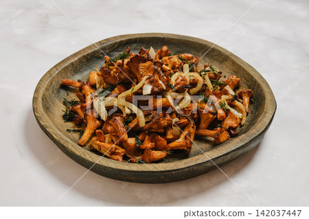 Mushroom dish served on wooden plate with onion and herbs after cooking 142037447