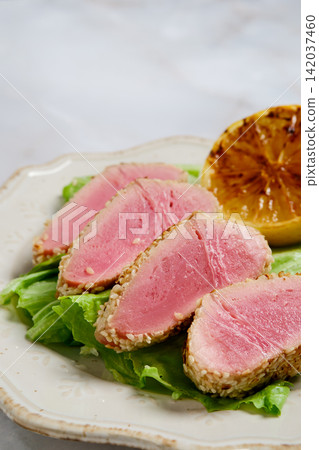 Seared tuna slices with sesame crust and grilled lemon on lettuce Seared tuna slices with sesame crust and grilled lemon on lettuce 142037460