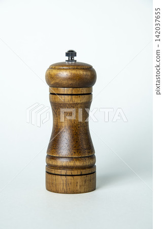A still life of kitchen tools: a wooden pepper mill standing against a white background. A still life of kitchen tools: a wooden pepper mill standing against a white background. 142037655