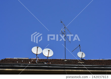 Satellite dishes and tv antenna on a roof against blue sky Satellite dishes and tv antenna on a roof against blue sky 142037813