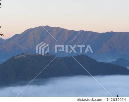 Takeda Castle Ruins floating above a sea of clouds and mountain ranges bathed in the morning sun. Takeda Castle Ruins floating above a sea of clouds and mountain ranges bathed in the morning sun. 142039034