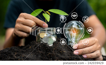 Energy saving light bulb and tree growing on stacks of coins on nature background. Saving, accounting and financial concept. Energy saving light bulb and tree growing on stacks of coins on nature background. Saving, accounting and financial concept. 142039429