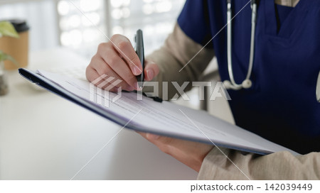Medical professional in navy scrubs writing patient notes on clipboard in modern hospital clinic Medical professional in navy scrubs writing patient notes on clipboard in modern hospital clinic 142039449