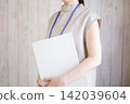 A woman standing with a binder file in her hand. 142039604