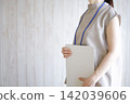 A woman standing with a binder file in her hand. 142039606
