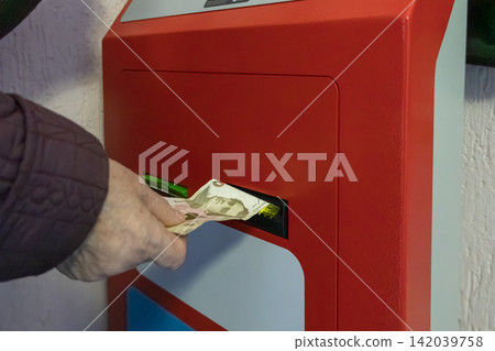A hand inserts paper currency into a bright red electronic terminal, emphasizing secure financial transactions and automated banking services for modern personal money management goals A hand inserts paper currency into a bright red electronic terminal, emphasizing secure financial transactions and automated banking services for modern personal money management goals 142039758