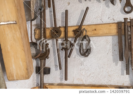 A collection of vintage metal tap and die threading tools hangs neatly on a wooden workshop wall, emphasizing industrial heritage and mechanical repair tasks for DIY manual projects A collection of vintage metal tap and die threading tools hangs neatly on a wooden workshop wall, emphasizing industrial heritage and mechanical repair tasks for DIY manual projects 142039791