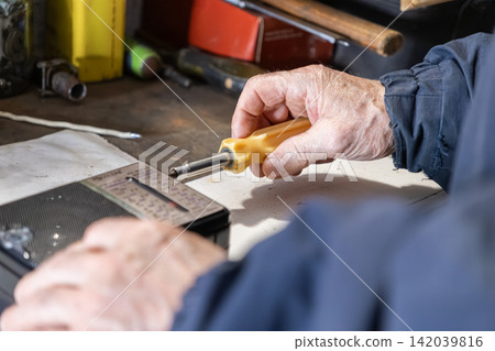 An elderly person uses a yellow screwdriver to repair a vintage portable radio on a cluttered workbench, reflecting skilled maintenance and hobbyist precision in a rustic workshop An elderly person uses a yellow screwdriver to repair a vintage portable radio on a cluttered workbench, reflecting skilled maintenance and hobbyist precision in a rustic workshop 142039816