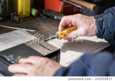 An elderly person uses a screwdriver to repair a vintage radio on a workshop bench, illustrating technical expertise and heritage craft skills in a detailed hobbyist fixing activity An elderly person uses a screwdriver to repair a vintage radio on a workshop bench, illustrating technical expertise and heritage craft skills in a detailed hobbyist fixing activity 142039817