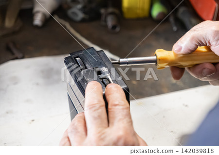 A skilled technician repairs an old portable radio with a yellow screwdriver, performing precise manual maintenance work on electronic equipment to restore vintage audio gear 142039818