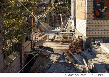 A construction site beside a suburban house with scattered bricks and wooden planks, depicting home renovation progress and building maintenance work during a sunny day outdoor setting A construction site beside a suburban house with scattered bricks and wooden planks, depicting home renovation progress and building maintenance work during a sunny day outdoor setting 142039939