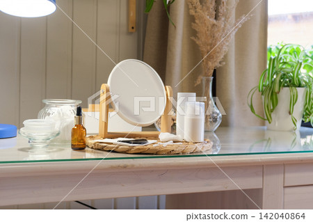 Vanity mirror with cream bottles, serum. Facial gua sha tool for skincare massage. Self care set desk. Feminine aesthetic. Beauty setting for selfcare routine. No people. Dressing table cosmetics 142040864