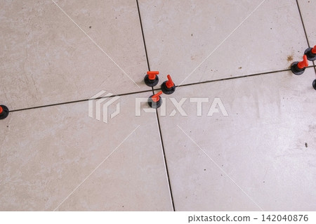 Worker Hand Laying Ceramic Tiles on the Floor. Repairman Placing White Gray Square Tiles, Applying Adhesive. Builder Installing Tile Using Leveler, Tile Leveling Clips. Tiling. Finishing Repair Work. 142040876