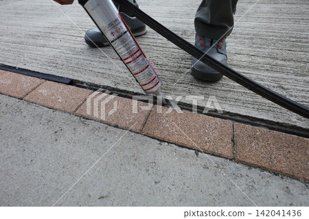 A worker repairs the joints between concrete and brick using a caulking gun. A worker repairs the joints between concrete and brick using a caulking gun. 142041436