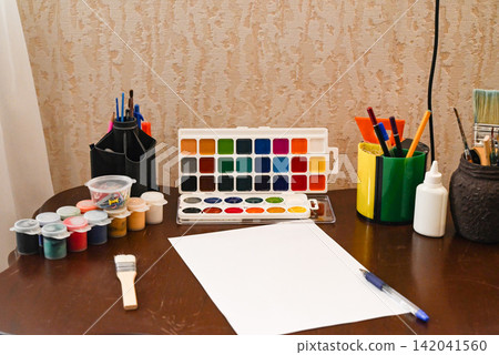 Creative workspace features painting supplies, brushes, and colorful materials ready for an art project at a desk Creative workspace features painting supplies, brushes, and colorful materials ready for an art project at a desk 142041560