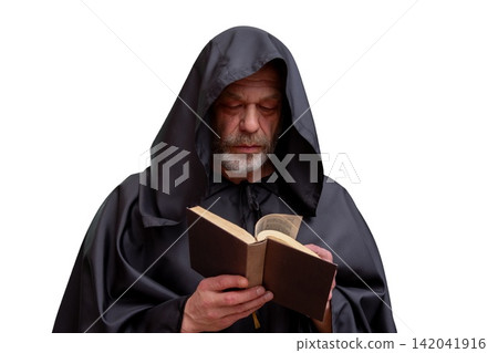 Isolated monk in black hooded robe reading an open book Isolated monk in black hooded robe reading an open book 142041916