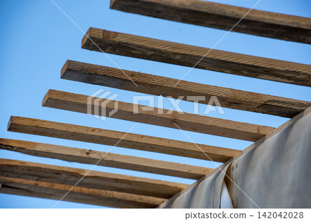Wooden planks forming a new roof structure from below, revealing the raw construction materials and blue sky, representing progress in building and development 142042028