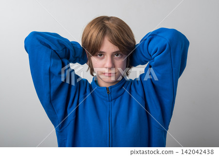 Young person looking directly at the viewer with a neutral expression while wearing a blue fleece jacket and resting hands behind their head, portraying casual comfort and relaxed posture Young person looking directly at the viewer with a neutral expression while wearing a blue fleece jacket and resting hands behind their head, portraying casual comfort and relaxed posture 142042438