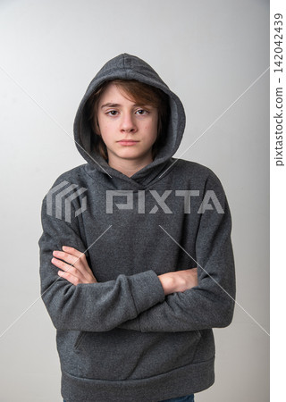 Young boy in a gray hoodie with arms crossed and a serious, pensive expression, conveying introversion, solitude and quiet contemplation against a plain background Young boy in a gray hoodie with arms crossed and a serious, pensive expression, conveying introversion, solitude and quiet contemplation against a plain background 142042439