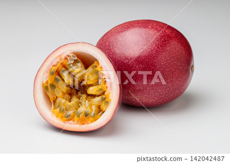 A photograph of one passion fruit from Kagoshima Prefecture and its halved cross-section against a white background. A photograph of one passion fruit from Kagoshima Prefecture and its halved cross-section against a white background. 142042487