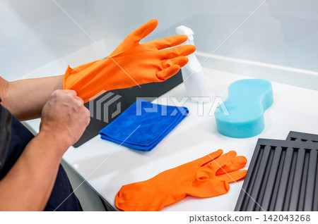 Hand putting on orange rubber gloves Hand putting on orange rubber gloves 142043268