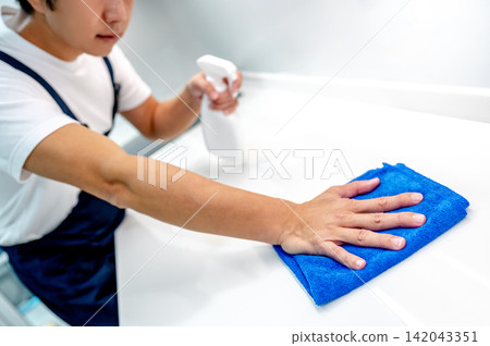 Asian male housekeeper holding spray bottle while wiping microfiber cloth on white countertop Asian male housekeeper holding spray bottle while wiping microfiber cloth on white countertop 142043351