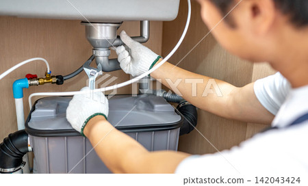 Male plumber with glove fixing pipe connection under kitchen sink with adjustable wrench Male plumber with glove fixing pipe connection under kitchen sink with adjustable wrench 142043424