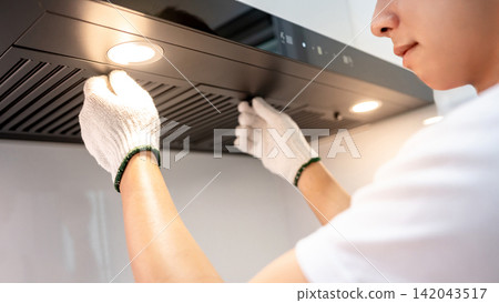 Asian male maintenance worker repairing modern cooker hood in domestic kitchen Asian male maintenance worker repairing modern cooker hood in domestic kitchen 142043517