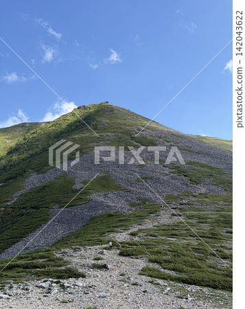 The mountaintop and the blue sky: A magnificent summer mountain landscape of the ridgeline leading to the summit and the hiking trail, set against a clear blue sky. The mountaintop and the blue sky: A magnificent summer mountain landscape of the ridgeline leading to the summit and the hiking trail, set against a clear blue sky. 142043622