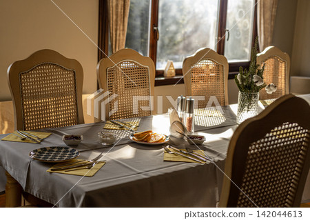 Dining table set with breakfast food wicker chairs and vase in bright sunlight Dining table set with breakfast food wicker chairs and vase in bright sunlight 142044613