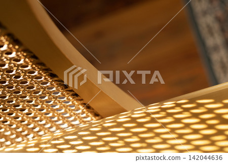 Woven rattan cane webbing casting geometric mesh shadow on wooden surface Woven rattan cane webbing casting geometric mesh shadow on wooden surface 142044636