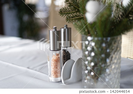 Stainless steel salt and pepper mills on white tablecloth in restaurant interior Stainless steel salt and pepper mills on white tablecloth in restaurant interior 142044654