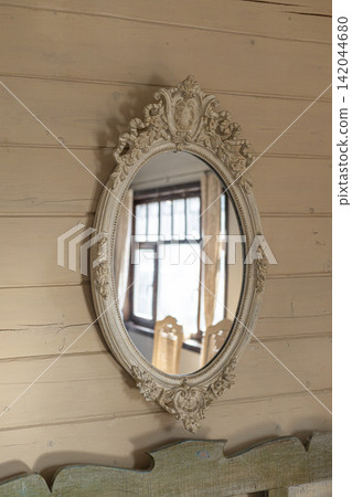 Vintage oval mirror with ornate carved frame hanging on wooden wall indoors Vintage oval mirror with ornate carved frame hanging on wooden wall indoors 142044680