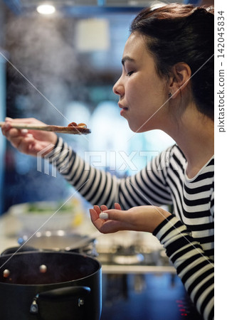 Woman, cooking and food with taste in kitchen for flavor, test and evaluation of ingredients. Home, nutrition and female person with spoon in hand for dinner, preparation and assessment of recipe Woman, cooking and food with taste in kitchen for flavor, test and evaluation of ingredients. Home, nutrition and female person with spoon in hand for dinner, preparation and assessment of recipe 142045834