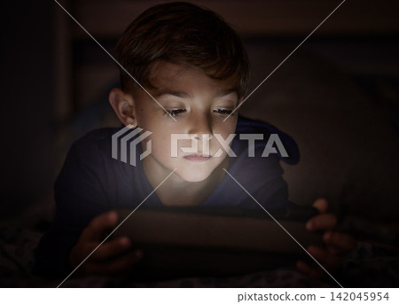 Tablet, relax and boy child in dark watching movie, film or show online for entertainment at home. Light, night and young kid streaming video on internet with digital technology in bedroom at house. Tablet, relax and boy child in dark watching movie, film or show online for entertainment at home. Light, night and young kid streaming video on internet with digital technology in bedroom at house. 142045954