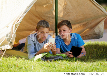 Phone, camping and boys in tent in nature streaming online movie, show or film on mobile app. Travel, technology and young teenagers relaxing on grass to scroll with cellphone on vacation or holiday. Phone, camping and boys in tent in nature streaming online movie, show or film on mobile app. Travel, technology and young teenagers relaxing on grass to scroll with cellphone on vacation or holiday. 142046178