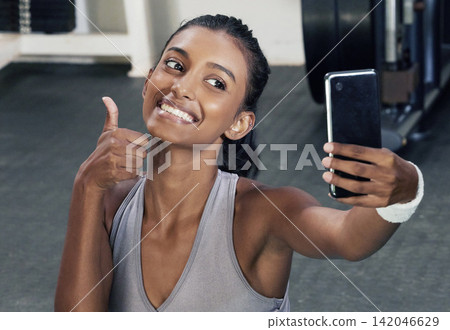 Woman, thumbs up and selfie on phone in gym for social media post or wellness blog in training. Happy, active and female person with mobile for sign of success workout or fitness session for health 142046629