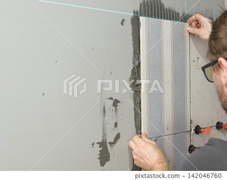 Worker Laying Ceramic Tiles on the Wall. Repairman Placing White Gray Square Tiles, Applying Adhesive. Builder Installing Tile Using Leveler, Tile Leveling Clips. Tiling. Finishing Repair Work. 4K Worker Laying Ceramic Tiles on the Wall. Repairman Placing White Gray Square Tiles, Applying Adhesive. Builder Installing Tile Using Leveler, Tile Leveling Clips. Tiling. Finishing Repair Work. 4K 142046760