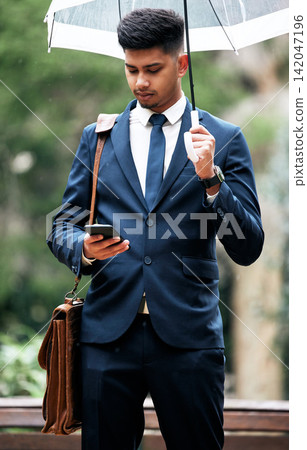 Businessman, umbrella and check smartphone in city for schedule, text or updates in calendar for work. Commuting in rain, man and outdoors in urban town with cell for social media, network and agenda Businessman, umbrella and check smartphone in city for schedule, text or updates in calendar for work. Commuting in rain, man and outdoors in urban town with cell for social media, network and agenda 142047196