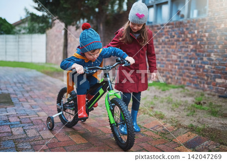 Girl, siblings and teaching with bicycle for ride, training wheels or hobby in outdoor activity in neighborhood. Little child or kid helping young brother on bike for playful cycling or trip at park Girl, siblings and teaching with bicycle for ride, training wheels or hobby in outdoor activity in neighborhood. Little child or kid helping young brother on bike for playful cycling or trip at park 142047269